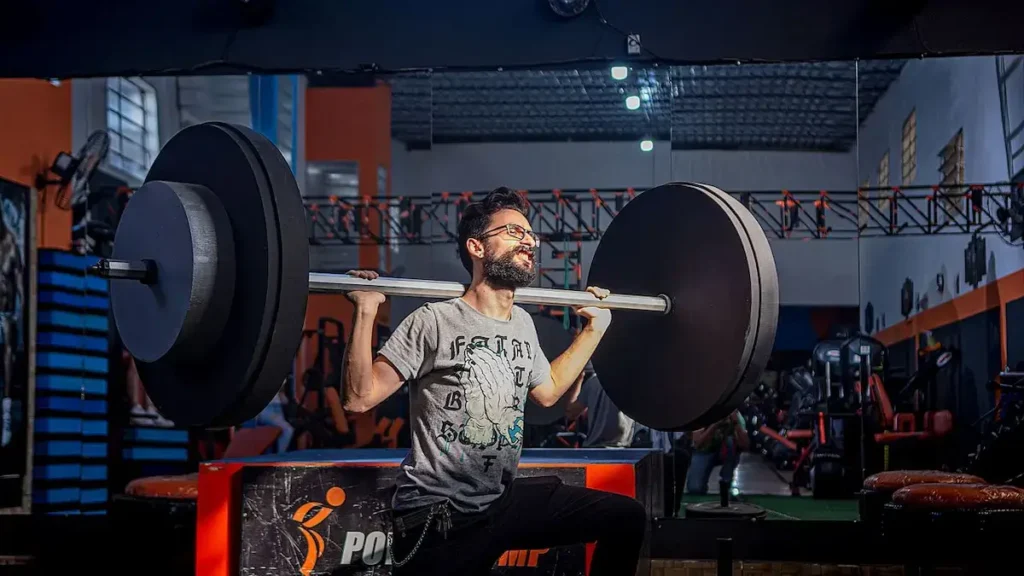 Homem a levantar peso com esforço máximo, ilustrando a tensão mecânica que desencadeia a hipertrofia muscular.